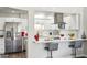Open concept kitchen with stainless appliances, bar seating, white cabinets, and stylish hood at 9926 W Lancaster Dr, Sun City, AZ 85351