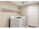 Modern laundry room with a side-by-side washer and dryer, shelving, and a white door at 7648 W Betty Elyse Ln, Peoria, AZ 85382