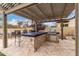 Outdoor kitchen with tile counter, built-in grill, under-counter storage beneath a pergola with backyard seating at 15936 W Bonitos Dr, Goodyear, AZ 85395