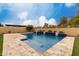 Beautiful backyard pool with stone waterfall feature, travertine decking, and lush landscaping with a clear blue sky above at 15936 W Bonitos Dr, Goodyear, AZ 85395
