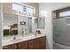 Bright bathroom with dual sinks, wooden vanity, framed mirrors, shower with glass door, and natural light at 15848 W Lahlum Ln, Surprise, AZ 85374