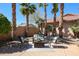Inviting backyard seating area with comfortable chairs and a table, surrounded by mature palm trees and desert landscaping at 16137 W Quail Creek Ln, Surprise, AZ 85374