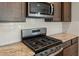 A close-up of a stainless steel gas range oven and microwave with white tiled backsplash and granite countertops at 16735 W Whispering Wind Dr, Surprise, AZ 85387