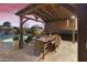 Outdoor dining area with a wood pergola, stone pavers, and seating beside the beautiful pool at 20594 S 194Th Pl, Queen Creek, AZ 85142