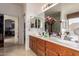 Bathroom with double sink vanity, mirrors, wooden cabinets, and decorative flowers and view to bedroom at 3588 S 257Th Ave, Buckeye, AZ 85326