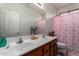 Bathroom with double sinks, mirror, wood cabinets, and a shower with a pink floral curtain at 3588 S 257Th Ave, Buckeye, AZ 85326