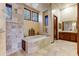 Luxurious bathroom featuring travertine tile, soaking tub, and natural light from multiple windows at 2430 S Geronimo Head Trl, Gold Canyon, AZ 85118