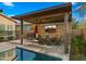 Inviting outdoor dining area with stone wall, TV, and poolside views under a modern pergola at 4462 S Frequency Dr, Mesa, AZ 85212