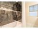 Modern bathroom showcasing a shower with dark marble-style tile, a white tub, and a window with natural light at 10018 N 103Rd Ave, Sun City, AZ 85351