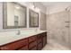 Bathroom with double sinks, wood cabinets, two framed mirrors, and a tiled walk-in shower at 46072 W Barbara Ln, Maricopa, AZ 85139