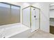 Bathroom featuring a white tub, gold trimmed glass shower, and a window with natural light at 6348 W Hill Ln, Glendale, AZ 85310