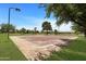 Outdoor basketball court with a standard hoop, painted lines, and shaded by trees, surrounded by green lawns at 19712 N Bridge Ct, Maricopa, AZ 85138