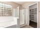 A bright bathroom with a glass-block window, shower, bathtub, and entrance to the walk in closet at 4481 N Luna W Rd, Litchfield Park, AZ 85340