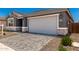 View of the two-car garage, gray exterior, stone facade, and brick paver driveway and a well-maintained lawn at 40531 W Michaels Dr, Maricopa, AZ 85138