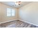 A bright bedroom with wood-look flooring, a ceiling fan, and a window with blinds for natural light at 44383 W Windrose Dr, Maricopa, AZ 85138