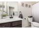 Well-lit bathroom featuring a single vanity with dark cabinets, framed art, and a toilet with a basket on top at 18069 W Tina Ln, Surprise, AZ 85387