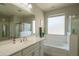 Bright bathroom features a bathtub, shower, and sink with white cabinets, plus plenty of natural light from a large window at 18187 W Via Montoya Dr, Surprise, AZ 85387