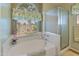 Bathroom with a soaking tub, glass-enclosed shower, and natural light from a window with decorative curtains at 18886 N 77Th Ave, Glendale, AZ 85308