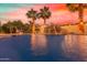 Backyard pool view featuring mature palm trees and a rock waterfall feature at sunset at 8260 N Buena Vista Dr, Casa Grande, AZ 85194