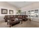 Cozy living room features a plush leather sofa, vaulted ceilings, and bright windows with plantation shutters at 13516 W Windsor Blvd, Litchfield Park, AZ 85340