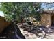 Shaded backyard featuring xeriscaping, a large shade tree, block wall fence, and air conditioning units at 43857 W Bedford Dr, Maricopa, AZ 85138