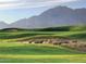 Picturesque golf course view with undulating green fairways, sand traps, and the backdrop of distant mountains at 43857 W Bedford Dr, Maricopa, AZ 85138