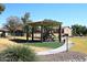 Community playground with a green turf, shade structure, and a variety of play equipment at 43857 W Bedford Dr, Maricopa, AZ 85138