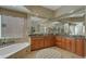 A luxurious bathroom with wood cabinets, granite counters, an oval tub, and a large mirror reflecting a separate powder room at 4235 W Harrison St, Chandler, AZ 85226
