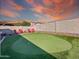 Landscaped backyard featuring artificial turf putting green, red Adirondack chairs, and a neutral colored privacy fence at 17346 W Lincoln St, Goodyear, AZ 85338