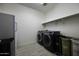 Well-lit laundry room with modern washer and dryer, shelving, storage, and a compact refrigerator at 40481 W Desert Fairways Dr, Maricopa, AZ 85138