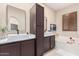 Well-lit bathroom with double sinks, tiled floors, and a large soaking tub with brown cabinetry at 12129 W Desert Mirage Dr, Peoria, AZ 85383