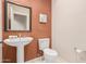 Cozy powder room with pedestal sink, toilet, and framed mirror over warm terracotta and cream color scheme at 12129 W Desert Mirage Dr, Peoria, AZ 85383