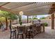 Outdoor kitchen and bar seating with built-in barbecue under a covered pergola at 3544 N 149Th Ave, Goodyear, AZ 85395