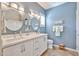 Bright bathroom featuring double sinks, white cabinets, decorative mirrors, and tiled floor at 19437 N Guardian Ln, Surprise, AZ 85387