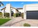 Stunning front exterior with arched windows, brick pathway, lush greenery, and a modern garage door at 8206 E Del Camino Dr, Scottsdale, AZ 85258