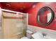 Red bathroom with a tiled shower, round mirror, toilet, and pedestal sink at 18256 N 75Th Ave, Glendale, AZ 85308