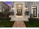 Stunning entryway with stone archway, flower filled planters, and decorative sconces at dusk at 10244 E Hualapai Dr, Scottsdale, AZ 85255