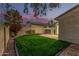 Charming backyard with lush grass, block wall and a patio under a colorful dusk sky at 619 E Jensen St # 80, Mesa, AZ 85203