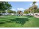 Backyard with tall trees, green grass, white block fence, and a play set at 2251 N 32Nd St # 10, Mesa, AZ 85213