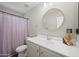 A well-lit bathroom showcasing a vanity sink with a round mirror and a bathtub with a purple shower curtain at 1244 E Princeton Ave, Gilbert, AZ 85234