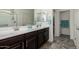 Bright bathroom featuring double sinks, dark wood cabinetry, walk-in shower, and tiled floors at 25983 W Escuda Dr, Buckeye, AZ 85396