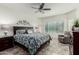 Cozy main bedroom showcasing a comfortable bed with floral bedding, ceiling fan and tiled floors at 25983 W Escuda Dr, Buckeye, AZ 85396