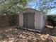 A backyard storage shed on a gravel lot, surrounded by trees and green foliage at 6834 E Culver St, Mesa, AZ 85207