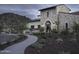 Elegant home exterior with stone facade, arched entryway, and desert landscaping, illuminated by stylish outdoor lighting at 18178 W Desert View Ln, Goodyear, AZ 85338