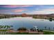 Picturesque lake view with palm trees, lakeside building, dock, and mountainous landscape under a colorful sky at 18178 W Desert View Ln, Goodyear, AZ 85338