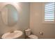 Powder room featuring a white pedestal sink, round mirror, toilet, and window with shutter at 18925 W Windsor Blvd, Litchfield Park, AZ 85340