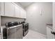 This laundry room features a modern washer and dryer, white tile flooring, and white cabinets at 5621 N 189Th Dr, Litchfield Park, AZ 85340