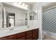 Well-lit bathroom featuring double sinks, a large mirror, and a shower-tub combo with a patterned shower curtain at 17574 W Corrine Dr, Surprise, AZ 85388