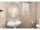 Powder room featuring a pedestal sink, toilet and a large oval mirror with natural light coming through the window at 35973 W Velazquez Dr, Maricopa, AZ 85138