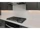 Close-up of a modern gas cooktop with quartz backsplash and dark cabinets in a bright kitchen at 26535 W Mcrae Dr, Buckeye, AZ 85396